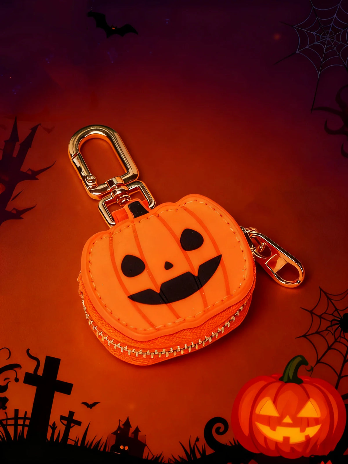 An orange carved pumpkin keychain accessory with a black face, set against a dark background with spiderwebs and bats.