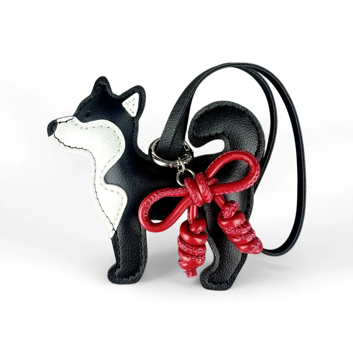 Colgante de perro Shiba Inu en blanco y negro con un lazo de cuero rojo trenzado a mano en una correa negra.