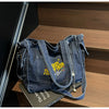 A dark denim women's crossbody bag with yellow embroidery resting on a wooden surface.