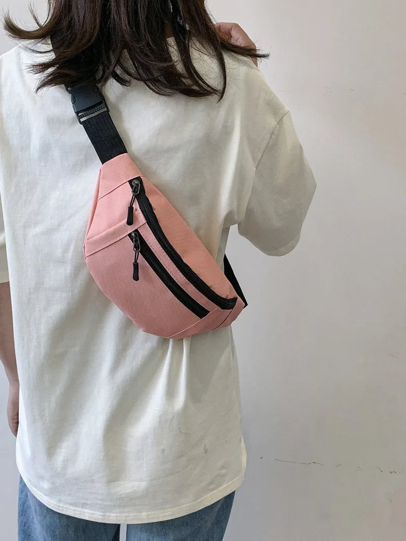 A pink nylon waist bag with black straps is worn on a white t-shirt.