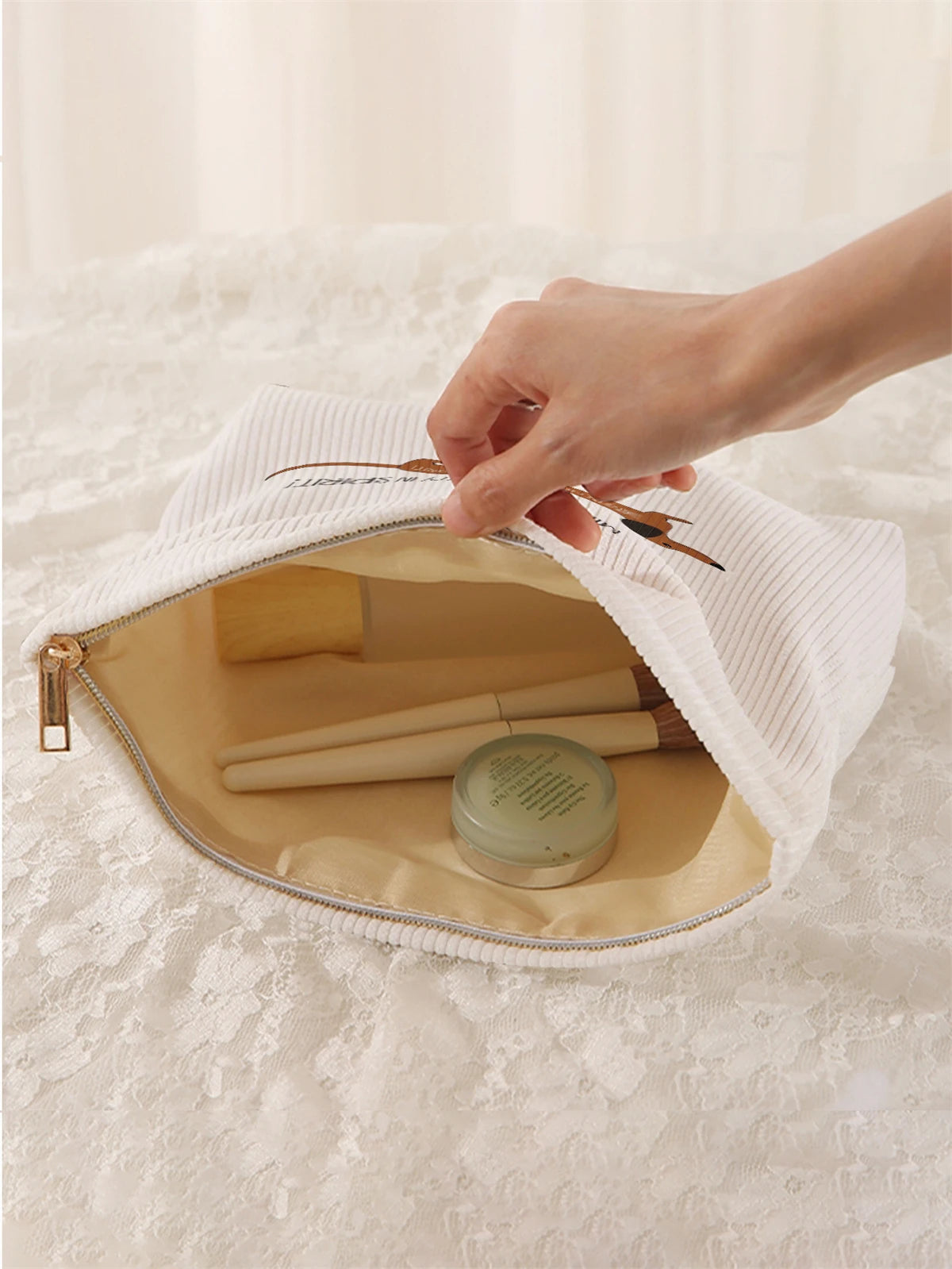 A hand is opening a white fabric storage bag with a zipper to reveal a beige interior holding makeup brushes.