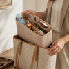 A person is holding a beige reusable felt handbag organizer pouch filled with various small items and a bottle.