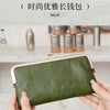 Eine Hand hält eine dunkel olivgrüne Lederclutch mit goldfarbener Schnalle.