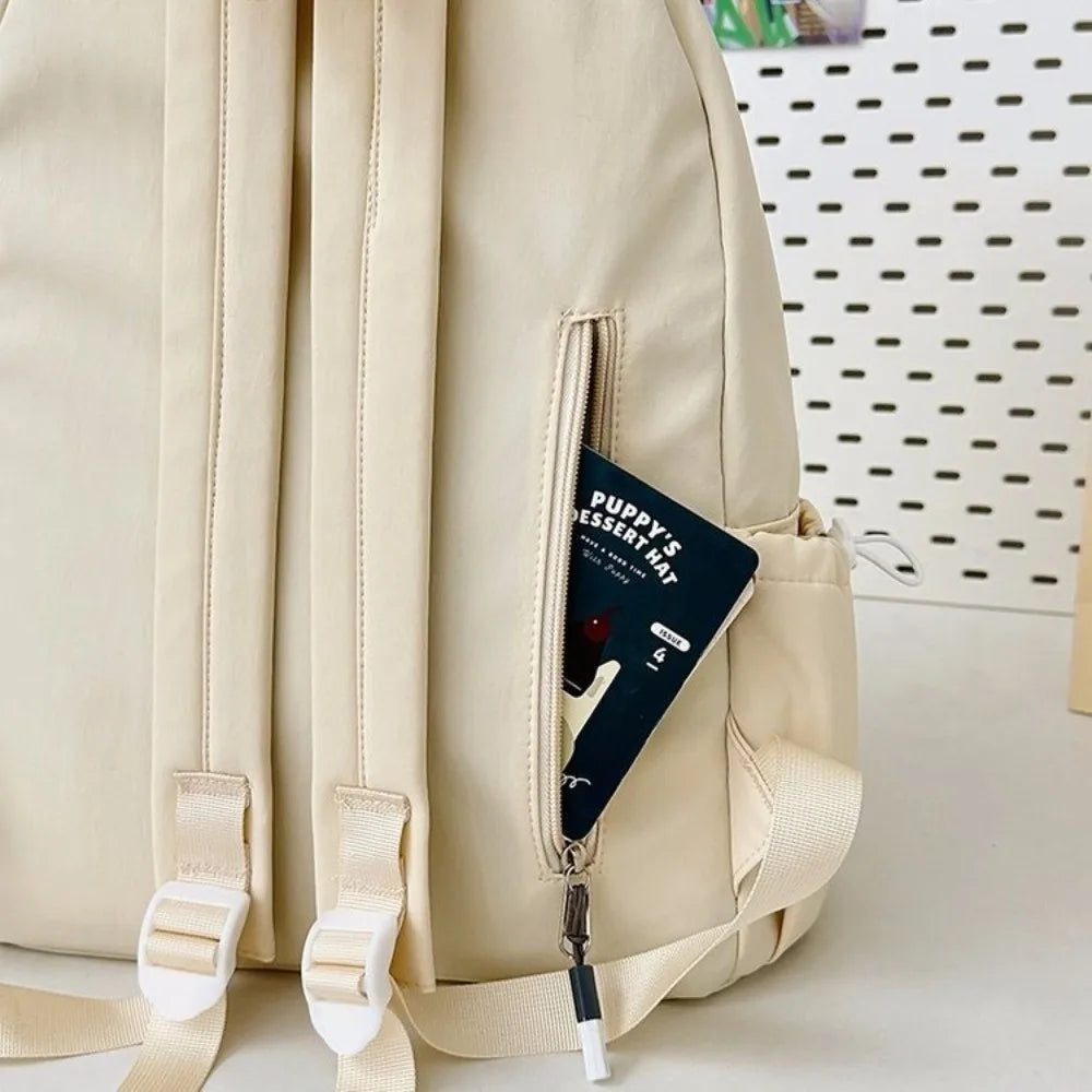 A light beige portable embroidered backpack with a zipper pocket and light tan straps.