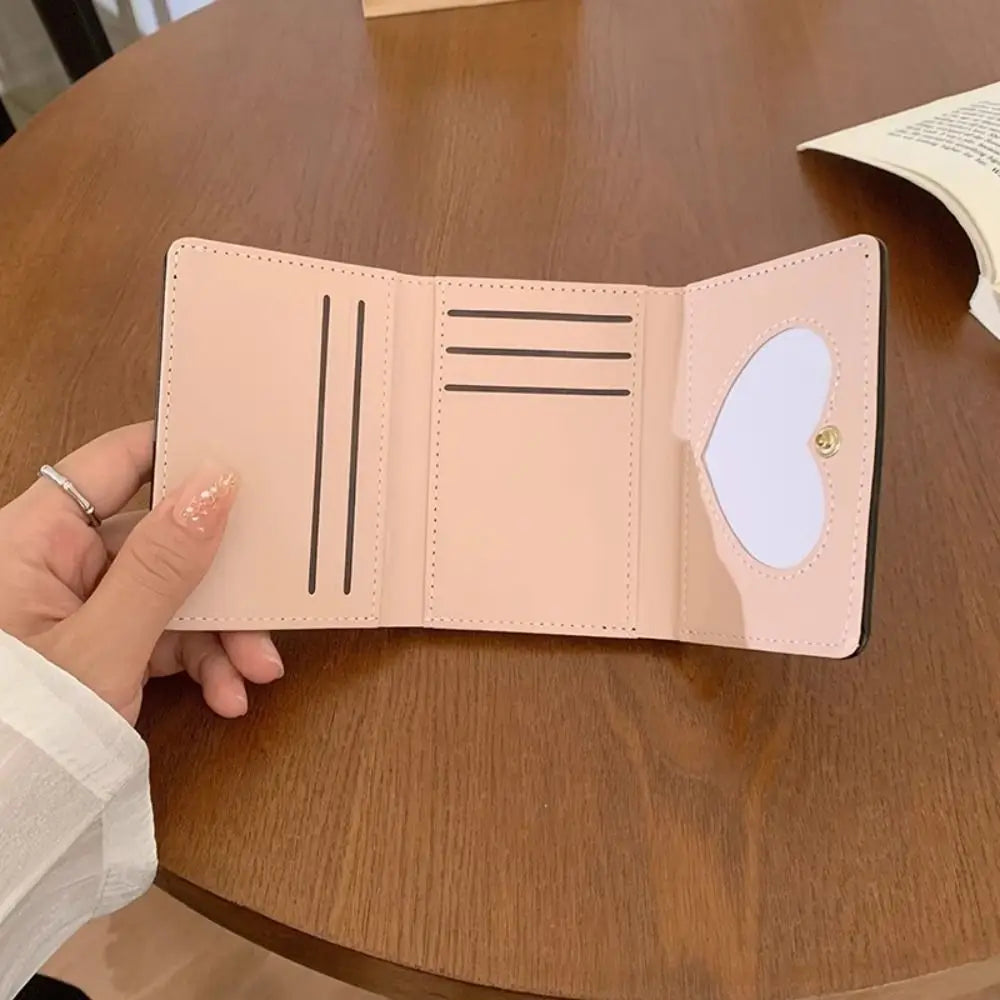 Cartera de cuero PU rosa claro plegable abierta sobre una mesa de madera.