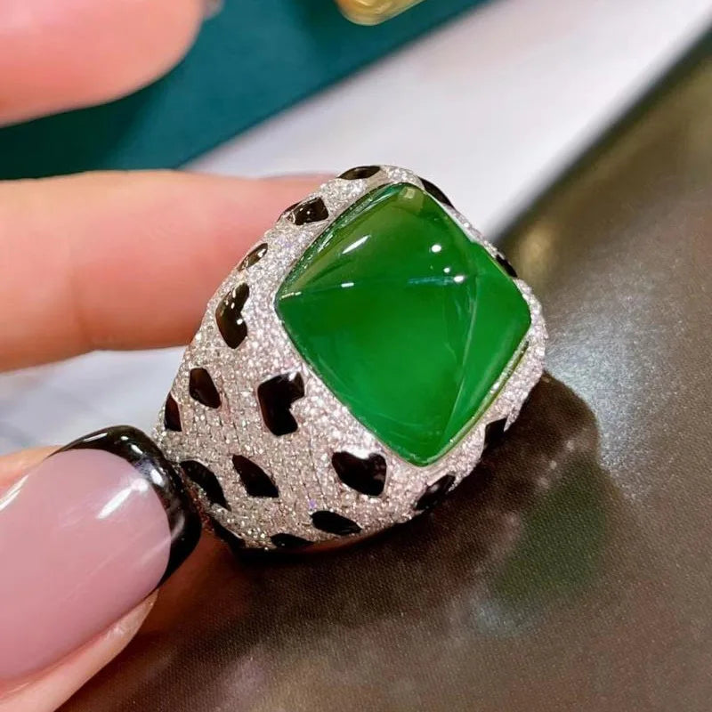 A close-up of a luxury leopard crystal statement ring featuring a vibrant green faceted gemstone set in a sparkling silver-to