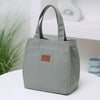 A gray durable aluminum foil insulated lunch bag with a leather patch logo resting on a white surface.