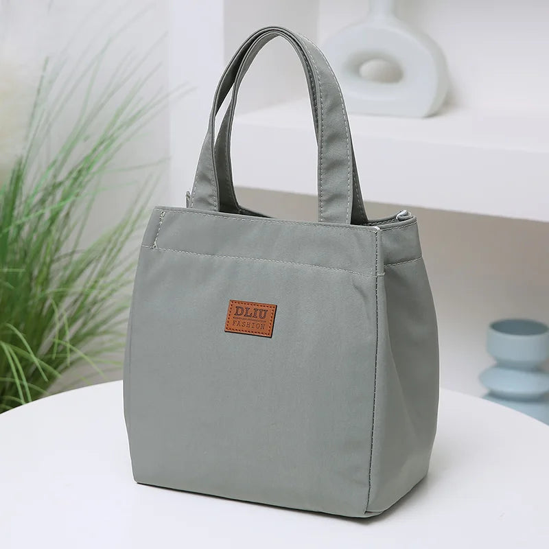 A gray durable aluminum foil insulated lunch bag with a leather patch logo resting on a white surface.