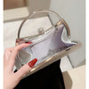A hand holds a silver pleated glitter evening handbag with a top handle and chain strap.