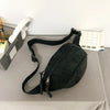 A black corduroy waist pack for women is displayed on a gray surface next to a white notepad.