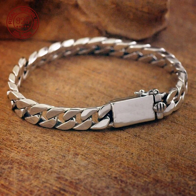 Sterling silver punk charm bracelet featuring a chain design and a padlock clasp resting on a wooden surface.