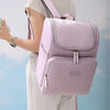 A person is wearing a light pink insulated travel backpack with gray straps and white pants.