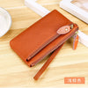A brown genuine leather wristlet clutch wallet with a zipper closure is shown on a wooden surface.