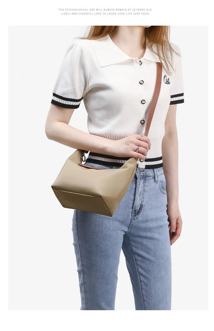 A young woman models a beige nylon dumpling crossbody shoulder bag with black trim and a brown strap.