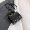 Black quilted leather crossbody handbag with gold chain accent resting on a gray blazer.