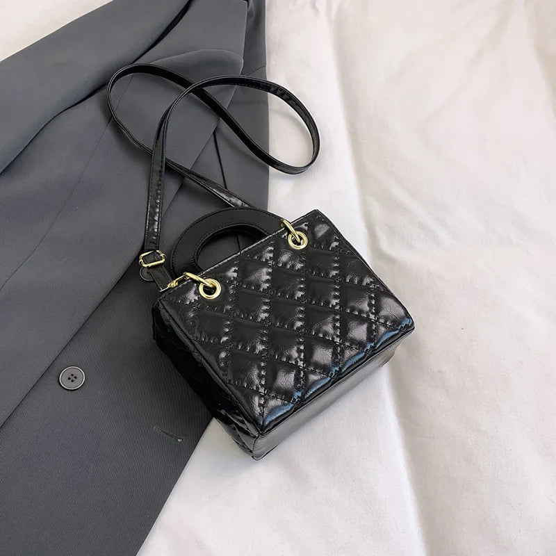 Black quilted leather crossbody handbag with gold chain accent resting on a gray blazer.