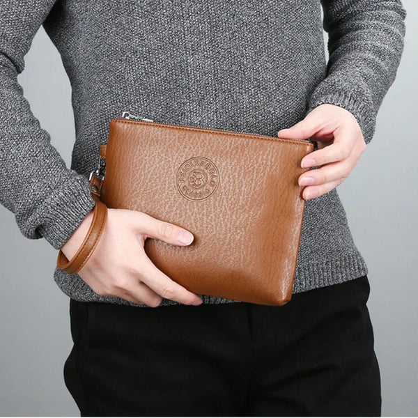 A person holds an elegant brown PU leather men's clutch wallet against a gray sweater and black pants.