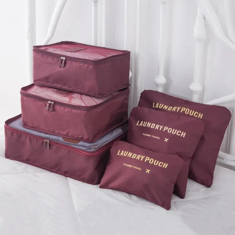 A set of three maroon laundry pouches and storage boxes for travel organization displayed on a white bed.
