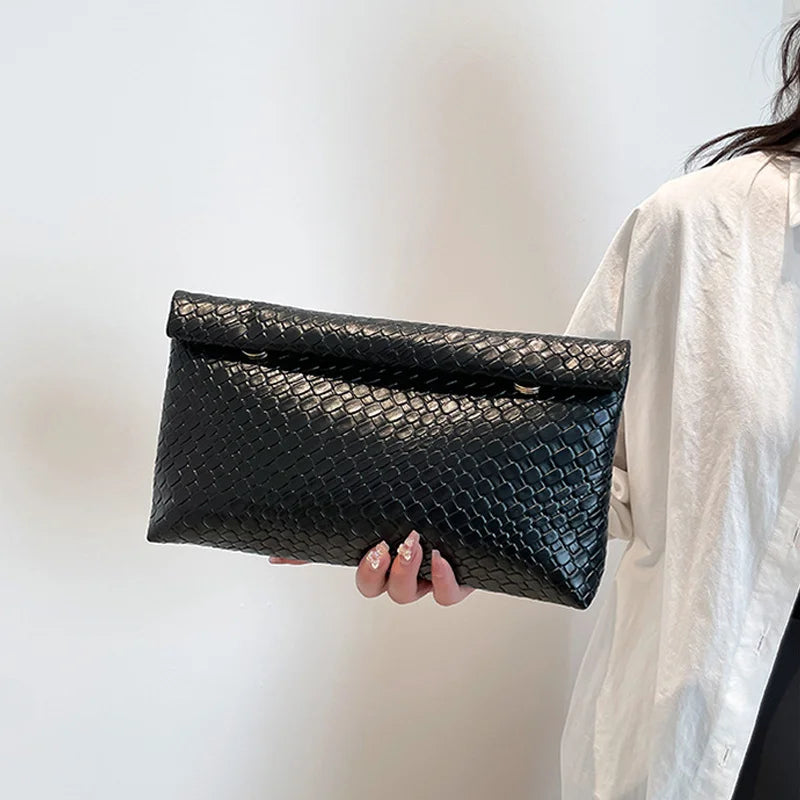Un bolso de mano negro tejido con textura sostenido por una persona contra un fondo blanco.