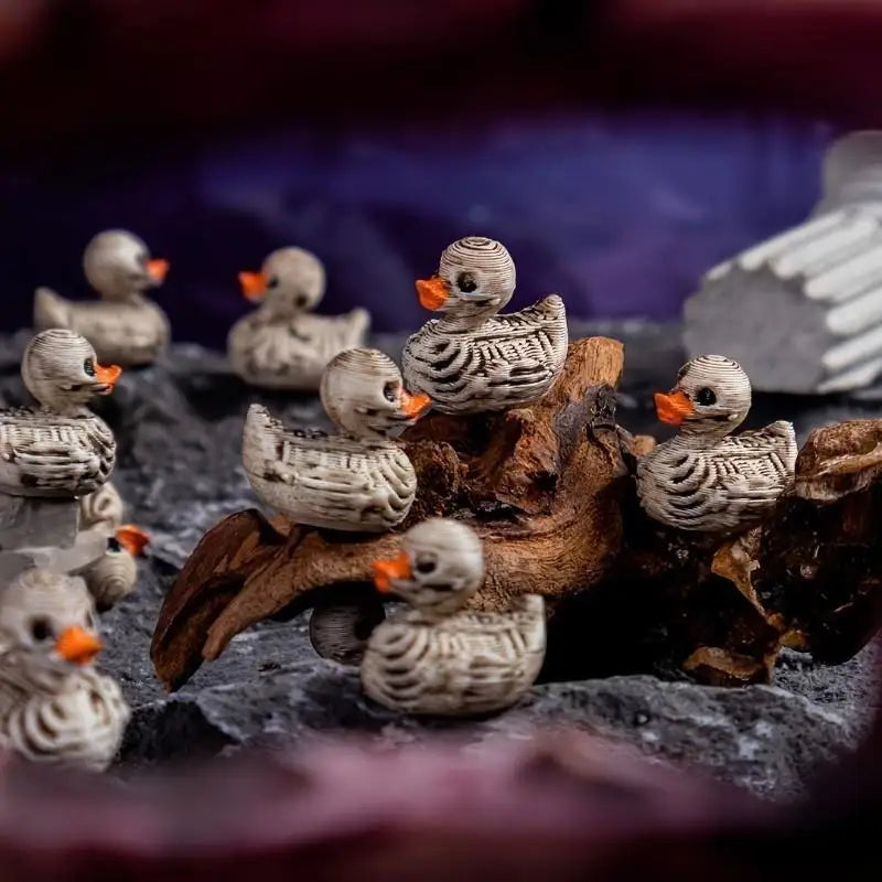 A collection of small, realistic duck figurines with mottled gray and brown feathers resting on dark rocks.