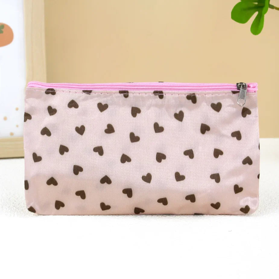 A light pink cosmetic bag with a zipper and a pattern of small brown hearts.