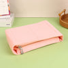 A pink felt cosmetic bag insert organizer lying on a green surface next to a woven basket and some boxed items.