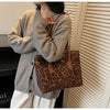 A woman is holding a brown leopard print vintage tote bag and a gray knit cardigan.