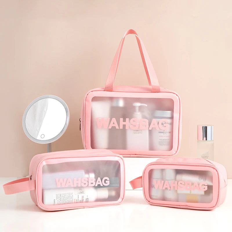 A pink clear waterproof travel toiletry bag with a handle and a matching compact mirror is displayed on a white surface.
