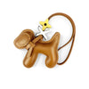 A tan PU leather puppy bag charm featuring a bow tie and a gold-colored charm attached to a brown leather strap.