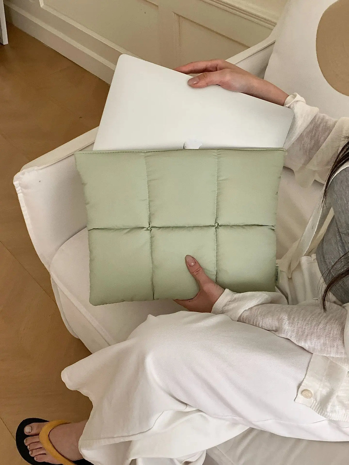 A person is holding a light green quilted laptop sleeve for a MacBook or PC inside a white chair.