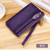 A dark purple genuine leather wristlet clutch wallet with a zipper closure resting on a wooden surface.