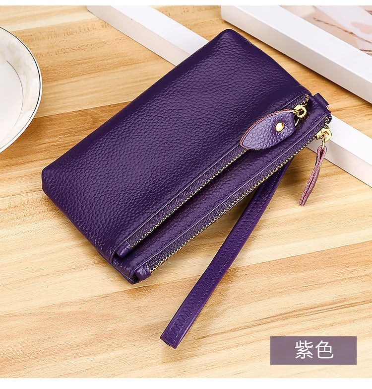 A dark purple genuine leather wristlet clutch wallet with a zipper closure resting on a wooden surface.