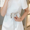 A person holds an elegant silver bowknot evening bag with a detachable chain strap against a white dress.