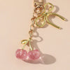 Collier en chaîne dorée avec pendentif cerise pailleté rose et un charm de nœud.