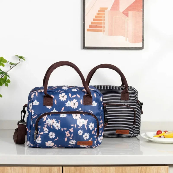 A blue floral patterned portable thermal lunch bag next to a striped black and white bag on a white countertop.