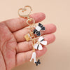 A hand holds a gold-toned enamel heart keychain featuring floral and butterfly charms.