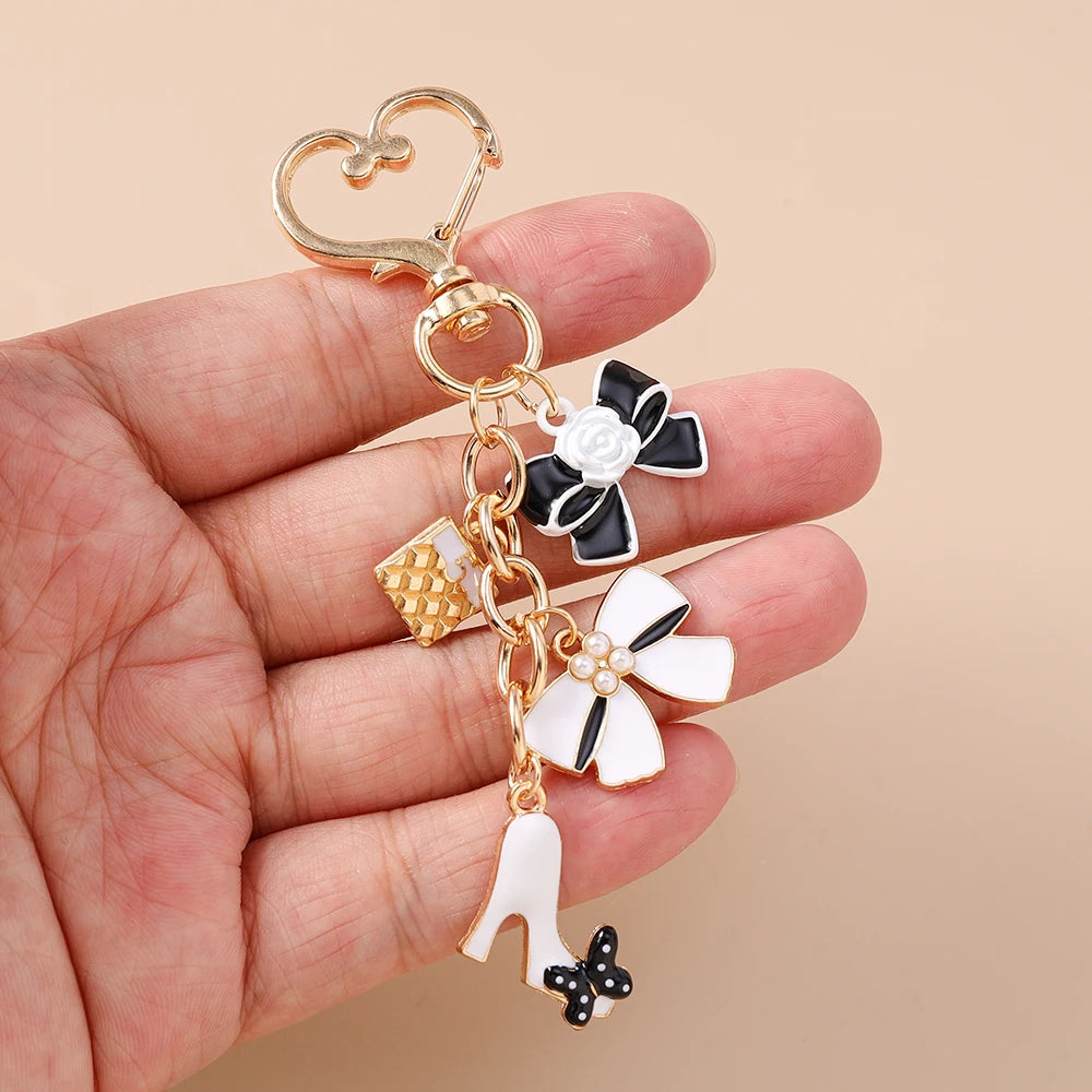A hand holds a gold-toned enamel heart keychain featuring floral and butterfly charms.