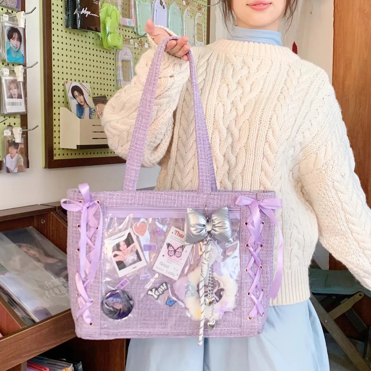 A woman holds a lavender transparent shoulder tote bag with a bow and decorative charms.
