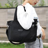 A woman holds a black durable nylon tote bag with a secure zipper closure against a blurred outdoor background.