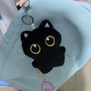Colgante de gato negro de peluche en llavero plateado, exhibido contra una bolsa de tela azul claro.