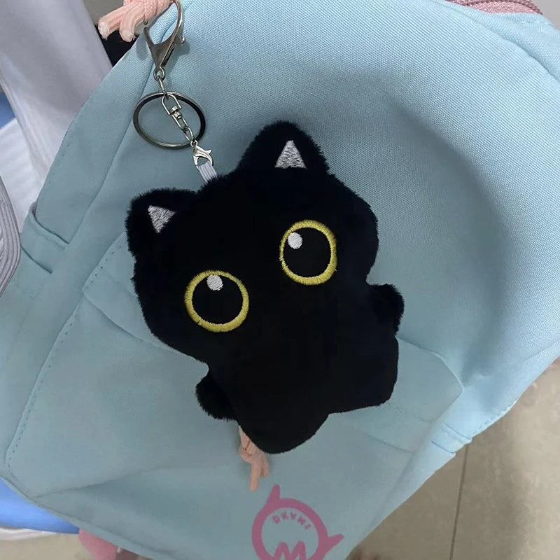 Colgante de gato negro de peluche en llavero plateado, exhibido contra una bolsa de tela azul claro.