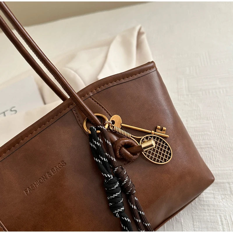 A brown leather tote bag with gold hardware and black braided straps resting on a white surface.