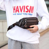 Un sac à taille en cuir véritable marron pour homme, tenu par une personne portant un sweat blanc.