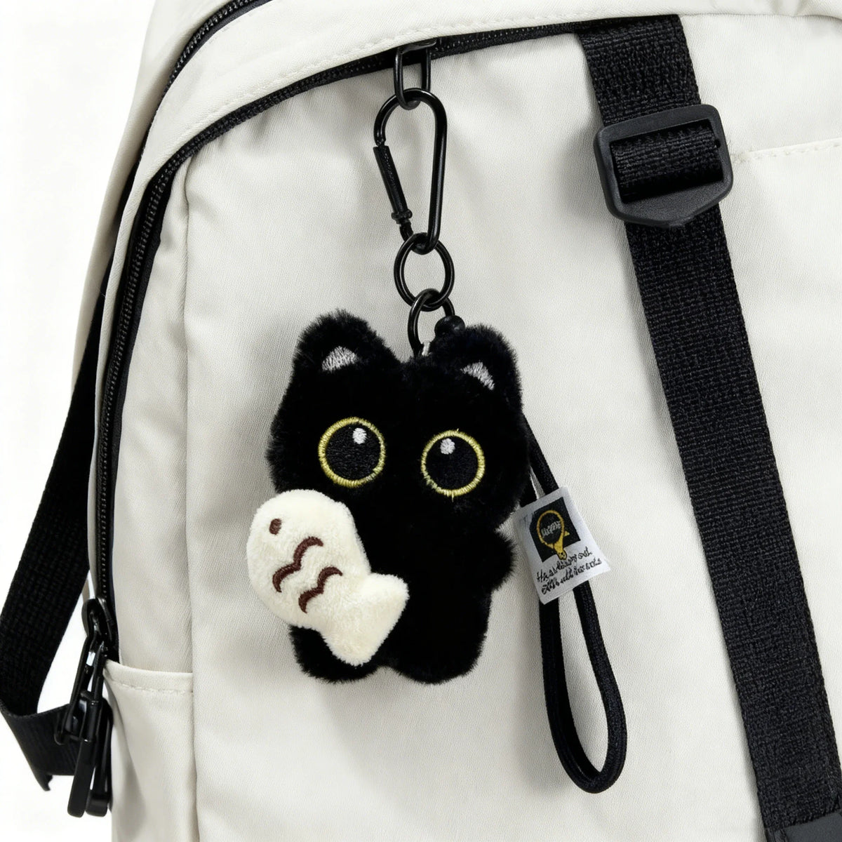 Black cat plush keychain charm attached to a white canvas bag strap.