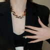 A close-up of a woman wearing a gold leopard print interlocking dangle necklace and a black blazer.