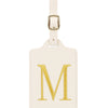 Étiquette de bagage rectangulaire en cuir beige avec un M brodé en or et une pince métallique argentée.