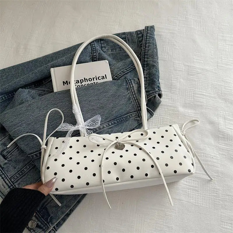 Weiße Leder-Schultertasche mit schwarzen Polka Dots und weißem Stoffgriff auf einer Jeansjacke.