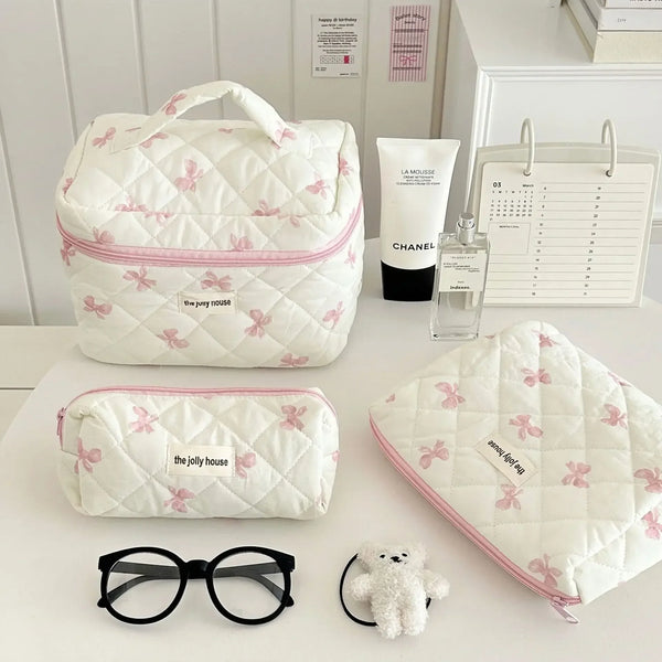 Collection de sacs de rangement cosmétiques rembourrés blancs avec motifs de nœuds roses, accompagnés de lunettes de soleil e