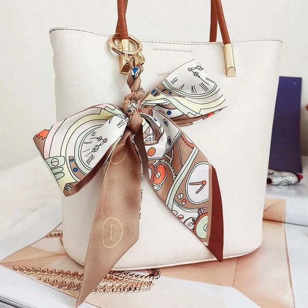 A white leather tote bag with a brown silk ribbon bow keychain attached.