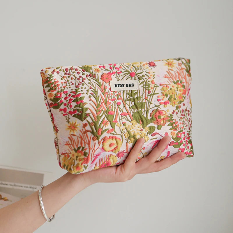 A hand holds a floral canvas makeup bag featuring pink, yellow, and green botanical prints.